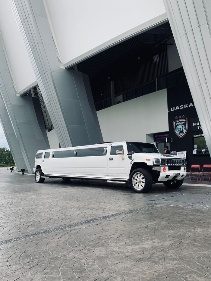 A sleek white limousine parked outside a contemporary building with geometric architecture.